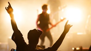 Illustrasjonsbilde: ser siluetten av en person som holder hendene i været på konsert. Ser scenen i bakgrunnen.