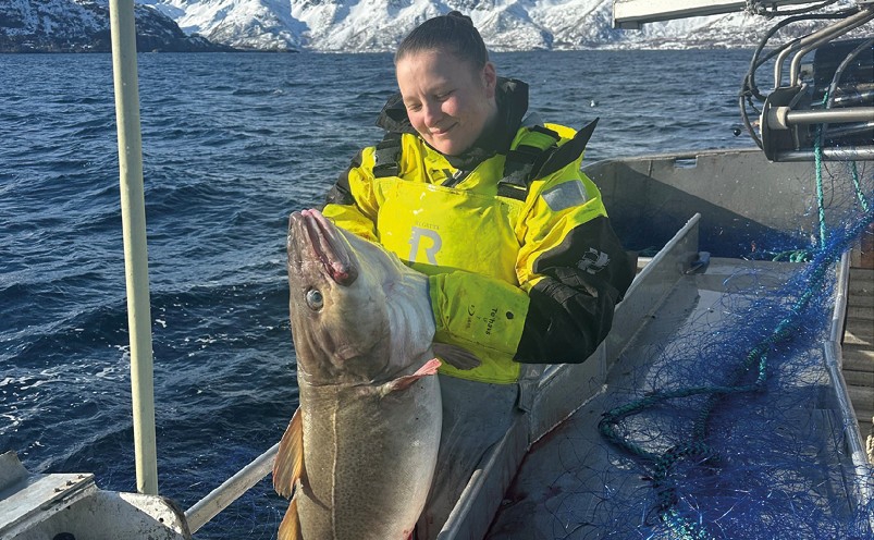 Dame på fiskebåt holder i en torsk