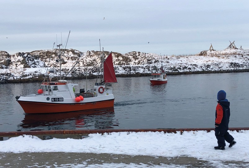 Barn på kai, fiskebåter på vei inn fra havet