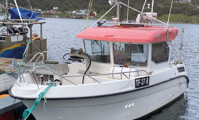 Litenn hvit fiskebåt med rød overbygg fortøyd ved kai i en havn. Båten har registreringsnummer TF-37-B og er utstyrt med fiskeredskaper og antenner på taket.
