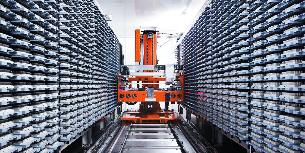 Fotografiet viser en automatisert biobank i form av bilde av en robot-lignende maskin som kjører mellom hyller som inneholder hundrevis av bokser med prøvemateriale.