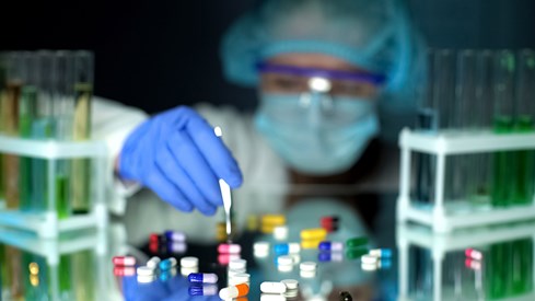 Labtekniker holder en pinsett og lener seg over noen piller