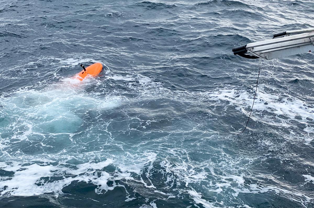 Foto viser HUGIN i havet. En liten del av H.U. Sverup er synelig til høyre på bildet. Havet er opprørt med bølger og hvitt skum.