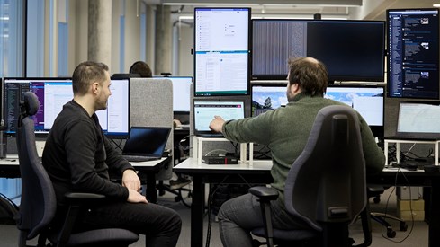 To menn på kontorstoler foran dataskjermer