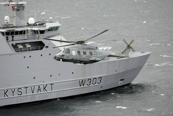 Photo of a helicopter flying in front of a coast guard ship.