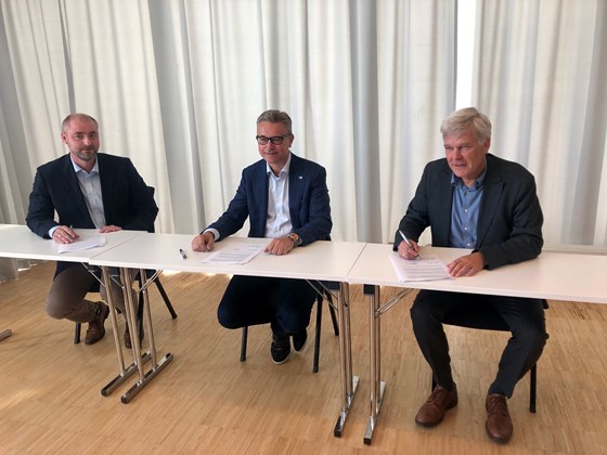 Tre personer ved et bord signerer en avtale.
