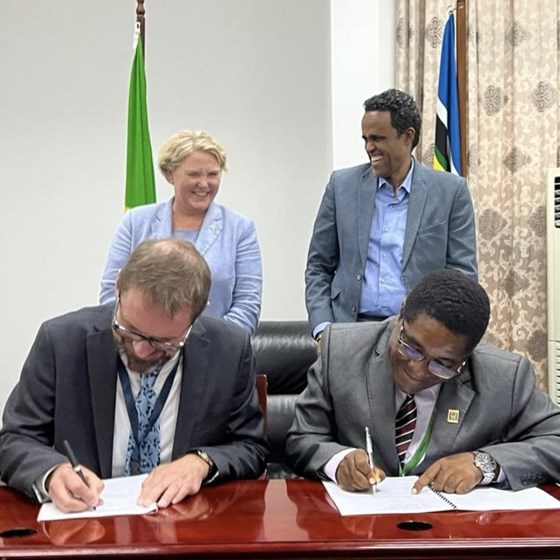 Bilete av Ragnar Pedersen (NIBIO) og Director General Geoffrey Mkamilo (TARI) sittande for å signere avtale. Utviklingsministeren og Tanzanias landbruksminister er ståande bak.