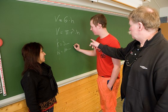 Elev skriver matteoppgave på tavlen. Lærer og medelev observerer.