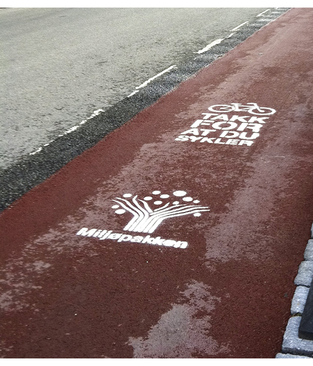 Figur 13.2 Sykkelfelt med farget asfalt gjennom Midtbyen i Trondheim. Den røde fargen markerer sykkelfeltet og gir et godt skille mellom sykkelveg og fortau samt vegbane. Det er hvit markering utenfor det røde feltet for å gi en ekstra tydelig avgrensing mot ve...