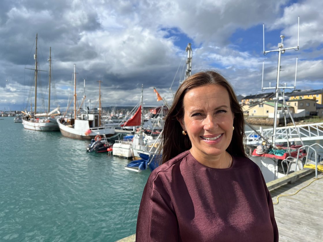 Bildet viser Fiskeri- og havminister Marianne Sivertsen Næss på kaia i Vadsø. Bildet viser fiskerbåter i bakgrunnen og statsråden foran. Anledningen er at regjeringen har en klar målsetting om økt bearbeiding av sjømat i Norge.