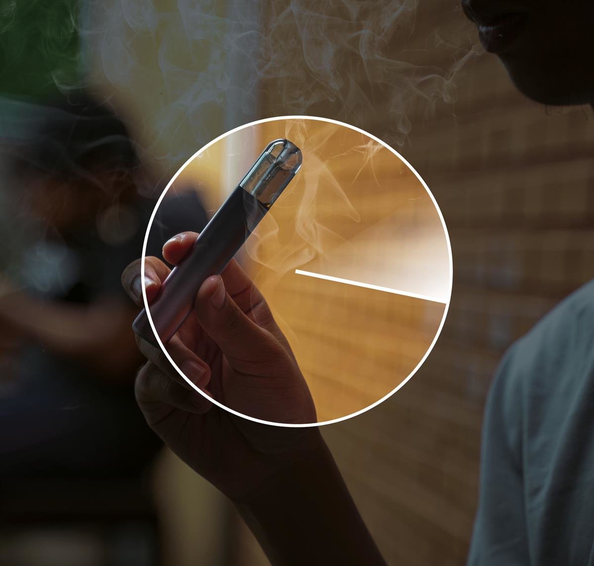 A person holds an e‑cigarette while smoke rises around the hand.