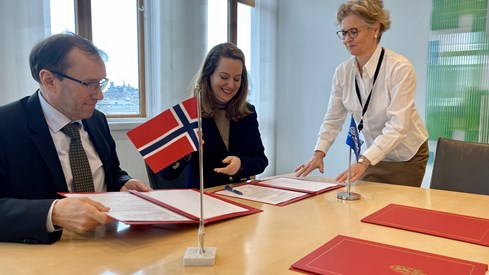Bilde av utenriksministeren og IOMs nye leder, Amy E. Pope, stittende for å signere avtale i hver sin protokoll