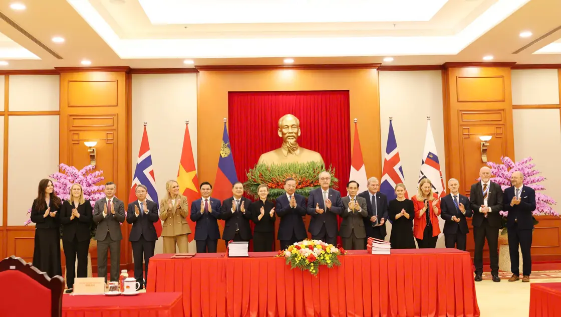 Representatives from the EFTA countries in Vietnam is posing for a photo in front of a line of flags