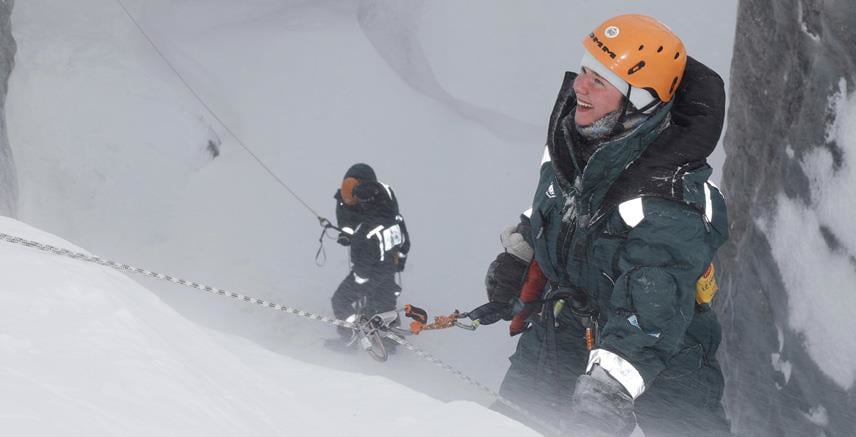 Brekurs i Ny-Ålesund. To forskere iført beskyttelsesdrakter og oransje hjelmer som klatrer med tau på isbre i snøvær. Foto: Stein Tronstad / NP.