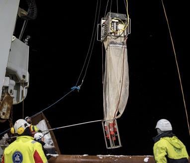 Fire forskere om bord på et skip i mørket. Et stort planktonnett heises opp med kran og en person manøvrerer nettet inn på dekk med tau, mens de andre ser på. Foto: Olaf Schneider / NP