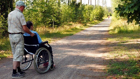 Eldre mann fører kvinne i rullestol