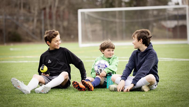Illustrasjonsbilde av tre barn som sitter på en kunstgressbane