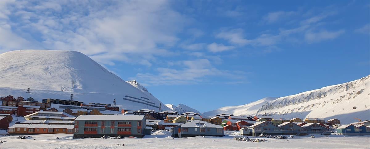 Bebyggelse med snøkledde fjell og blå himmel i bakgrunnen.