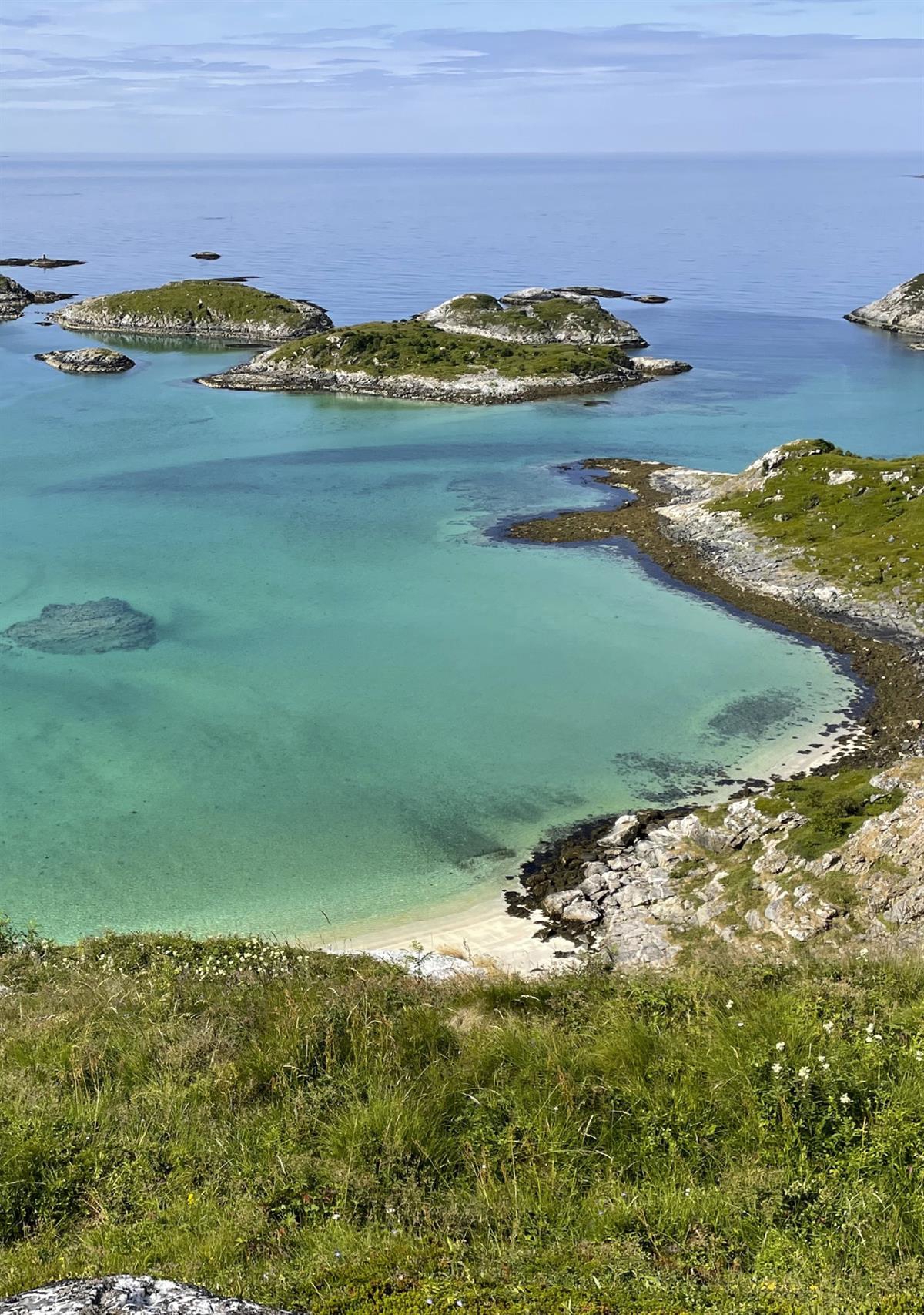 Små gresskledde øyer og sandstrender mot turkis og blått hav.