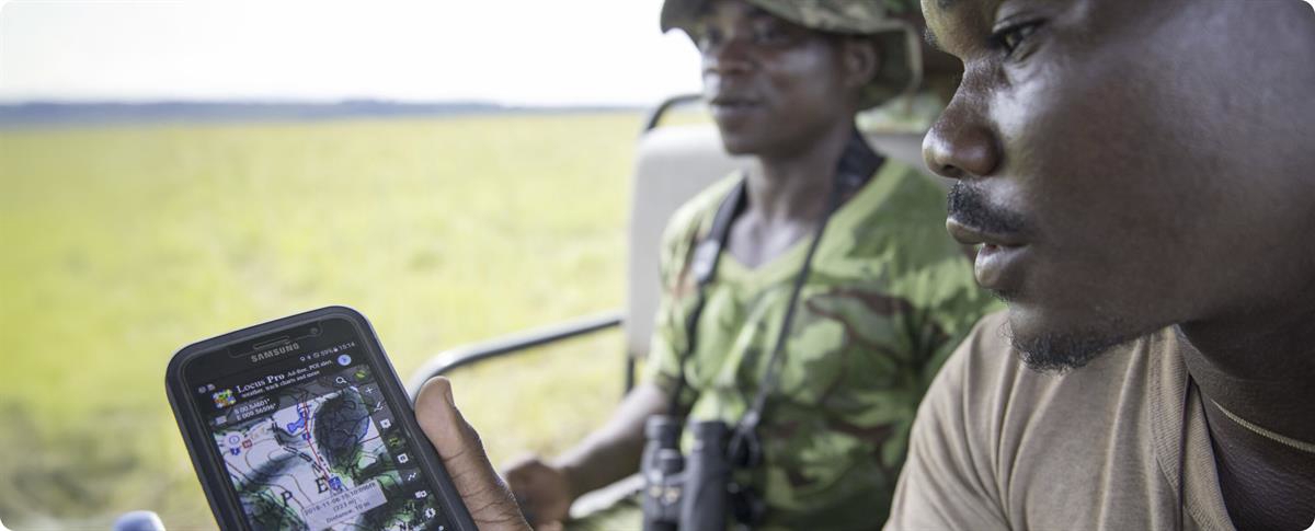 To personer i bil ser på kartapplikasjon på mobil med uklar natur i bakgrunnen.