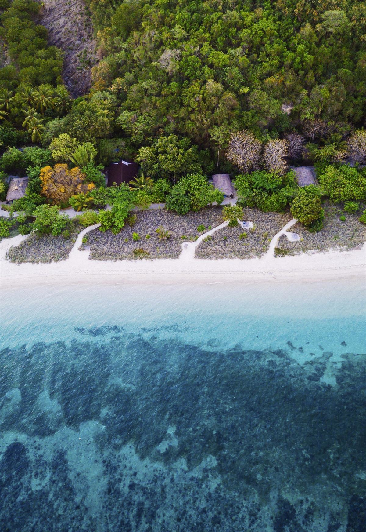 Tropisk skog og enkel bebyggelse langs hvite sandstrender med blått hav.
