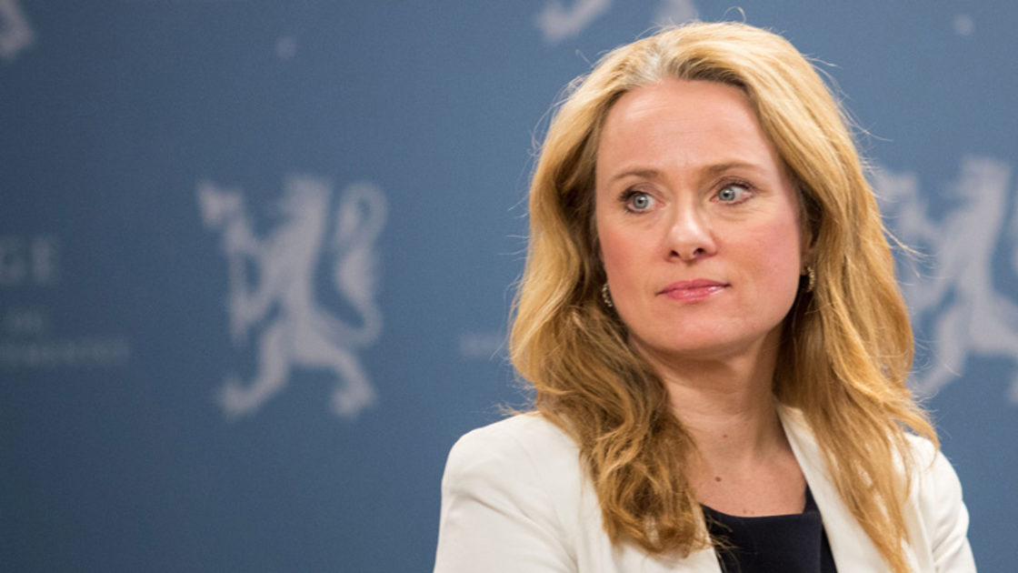 Arbeids- og sosialminister Anniken Hauglie foran blå pressevegg med Arbeids- og sosialdepartementets logo