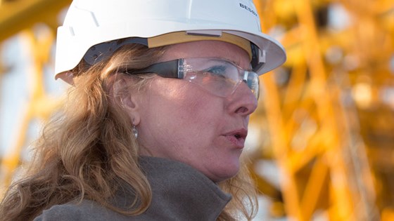Nærbilde av arbeids- og sosialminister Anniken Hauglie med hvit vernehjelm, med gul kranmast i bakgrunnen.