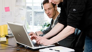 Bilde av to personer som samarbeider over en datamaskin.