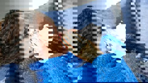 Kvinne som ligger på sofaen og som snyter seg i et papir