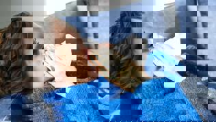 Kvinne som ligger på sofaen og som snyter seg i et papir