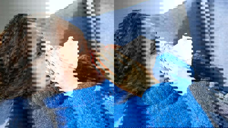 Kvinne som ligger på sofaen og som snyter seg i et papir