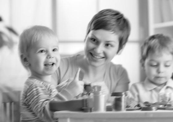 Kvinne som sitter og leker med to barn – sort/hvitt bilde