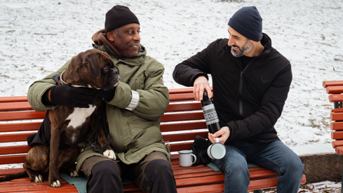 To menn og ein hund som sit på ein benk. 