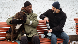 To menn og ein hund som sit på ein benk. 