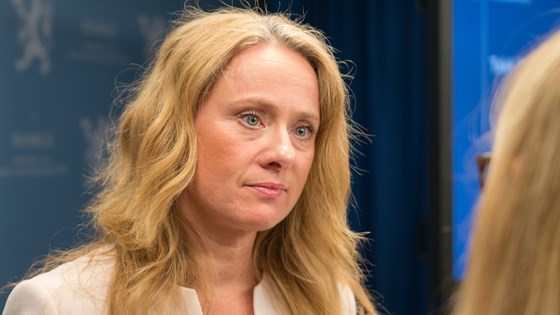 Arbeids- og sosialminister Anniken Hauglie foran blå pressevegg.