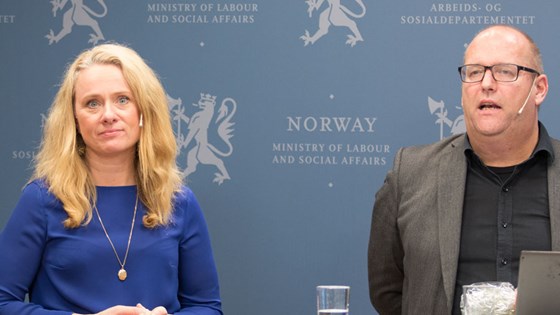 Arbeids- og sosialminister Anniken Hauglie i blå kjole til venstre, Ole Andreas Engen i grå dress og sort skjorte foran blå pressevegg med riksløven.