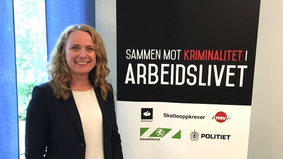 Anniken Hauglie (arbeids- og sosialminister) ved siden av plakat med teksten «Sammen mot kriminalitet i arbeidslivet» og logoene til Skatteetaten, Skatteoppkrever, Nav, Arbeidstilsynet og Politiet.