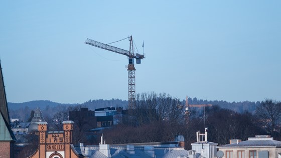 Byggekran i Oslo mot blå himmel og hustak.