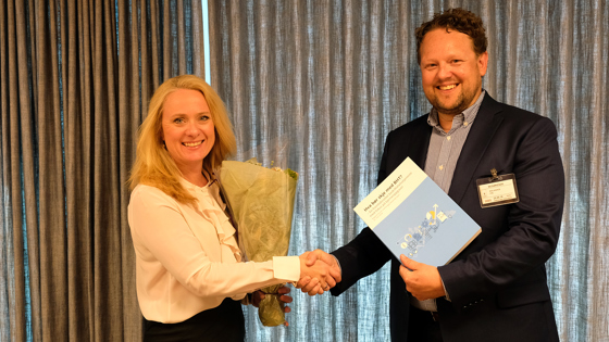 Anniken Hauglie med blomsterbukett (til venstre) og Pål Molander tar hverandre i hånden. Pål Molander med rapporten "Hva bør skje med BHT?" i hånden.