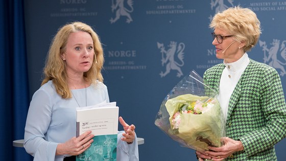 Anniken Hauglie og Anne Cathrine Frøstrup gir hverandre blomster og NOU om varsling, foran blå pressevegg