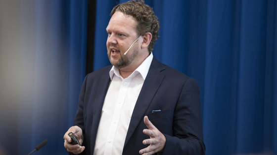 Pål Molander står og snakker foran blå gardin.