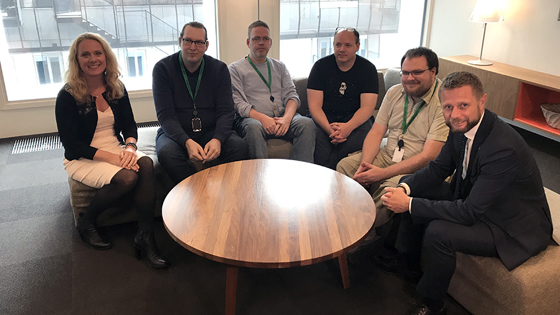 Anniken Hauglie og Bent Høie sammen med medarbeidere i Unicus, sittende i sofa ved et rundt bord.