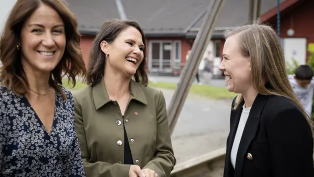 Tre statsråder som står like utenfor en barnehage og smiler.