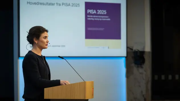 Kari Nessa Nordtun på talerstol. Presentasjon med hovedresultater fra PISA 2025 på skjerm i bakgrunnen.