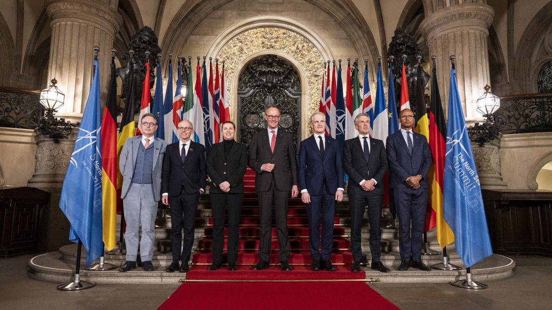 Gruppebilde med deltakere foran en rekke flagg.