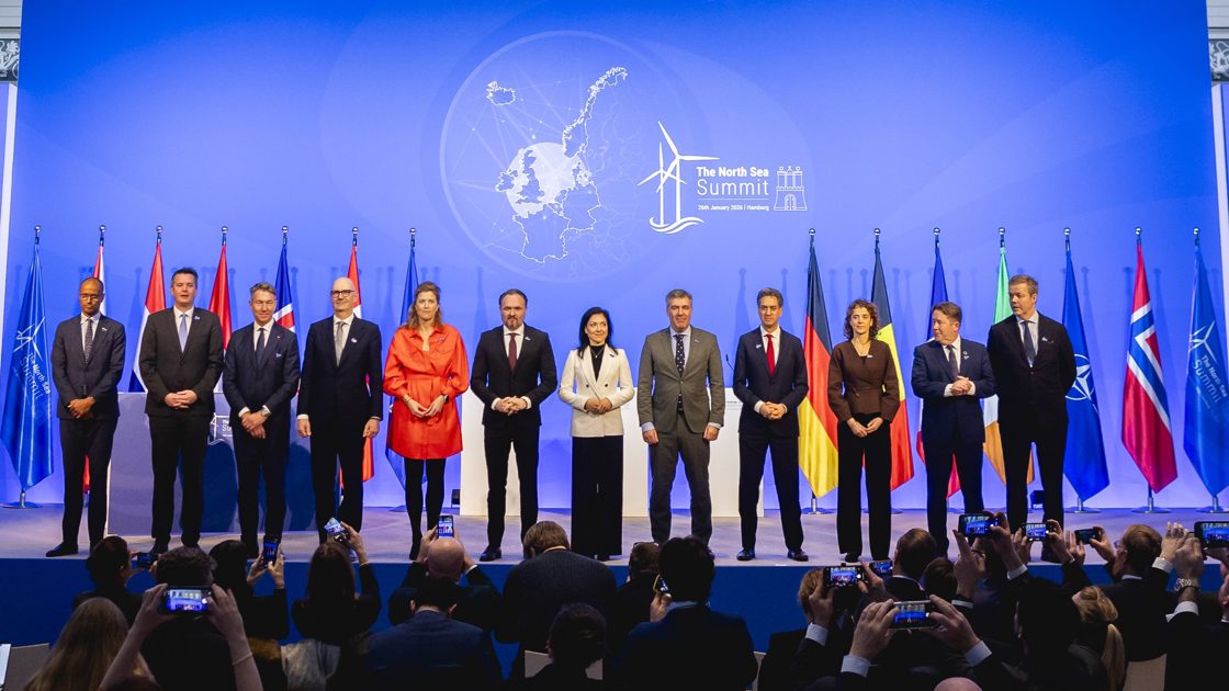 På bildet ser du en gruppe mennesker på scenen, foran en bakgrunn hvor det står "The North Sea Summit".