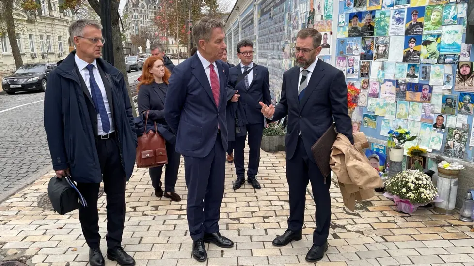 Vassdrags- og energidirektør Kjetil Lund, energiminister Terje Aasland og Norges ambassadør til Ukraina, Lars Ragnar Aalerud Hansen, foran minneveggen for de falne i Ukraina.