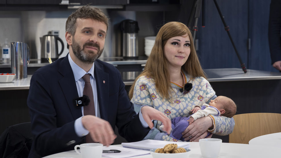 Helse- og omsorgsminister Jan Christian Vestre sit ved sidan av ei nybakt mor som held sonen sin i armane sine