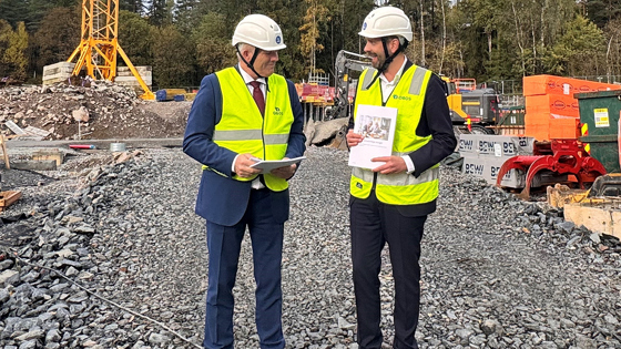 Helse- og omsorgsminister Jan Christian Vestre og kommunal- og distriktsminister Bjørnar Skjæran står på en byggeplass iført hjelmer og vester og holder begge en rapport i hendene