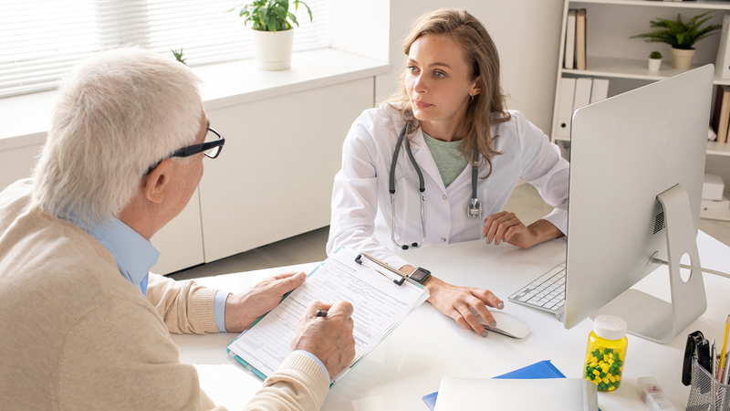 En kvinnelig fastlege i dialog med en eldre mannlig pasient